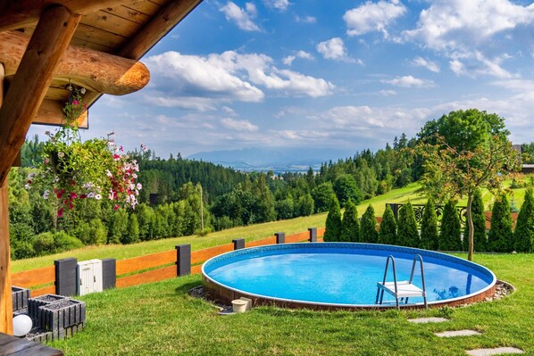 A circular swimming pool with a ladder, surrounded by a wooden deck and a grassy area with trees and mountains in the background. - Luxury Holiday Villa, Pool, Sauna, Jacuzzi (Nowy Targ)