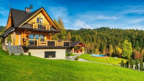 A log cabin with a stone foundation, a deck, a swimming pool, and a forested backdrop. - Luxury Holiday Villa, Pool, Sauna, Jacuzzi (Nowy Targ)