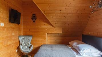 A cozy room with a bed, a chair, and a wooden ceiling.