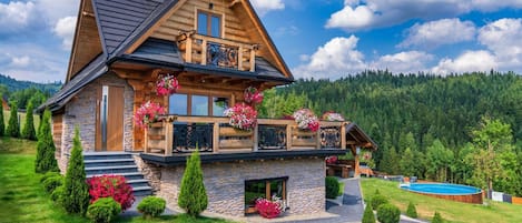 A log cabin with a stone foundation, a balcony with flower boxes, and a swimming pool.