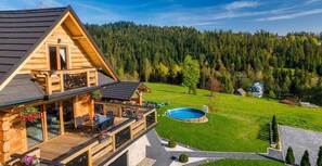 Eine Holzhütte mit Balkon, Schwimmbad und bewaldeter Landschaft.
