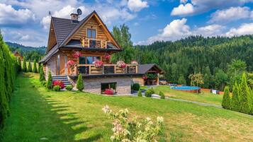 A wooden cabin with a balcony, surrounded by a well-maintained lawn and a pool.