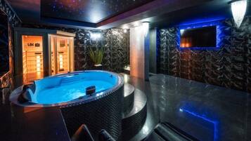 A modern indoor pool area with a hot tub, seating, and a stone wall.