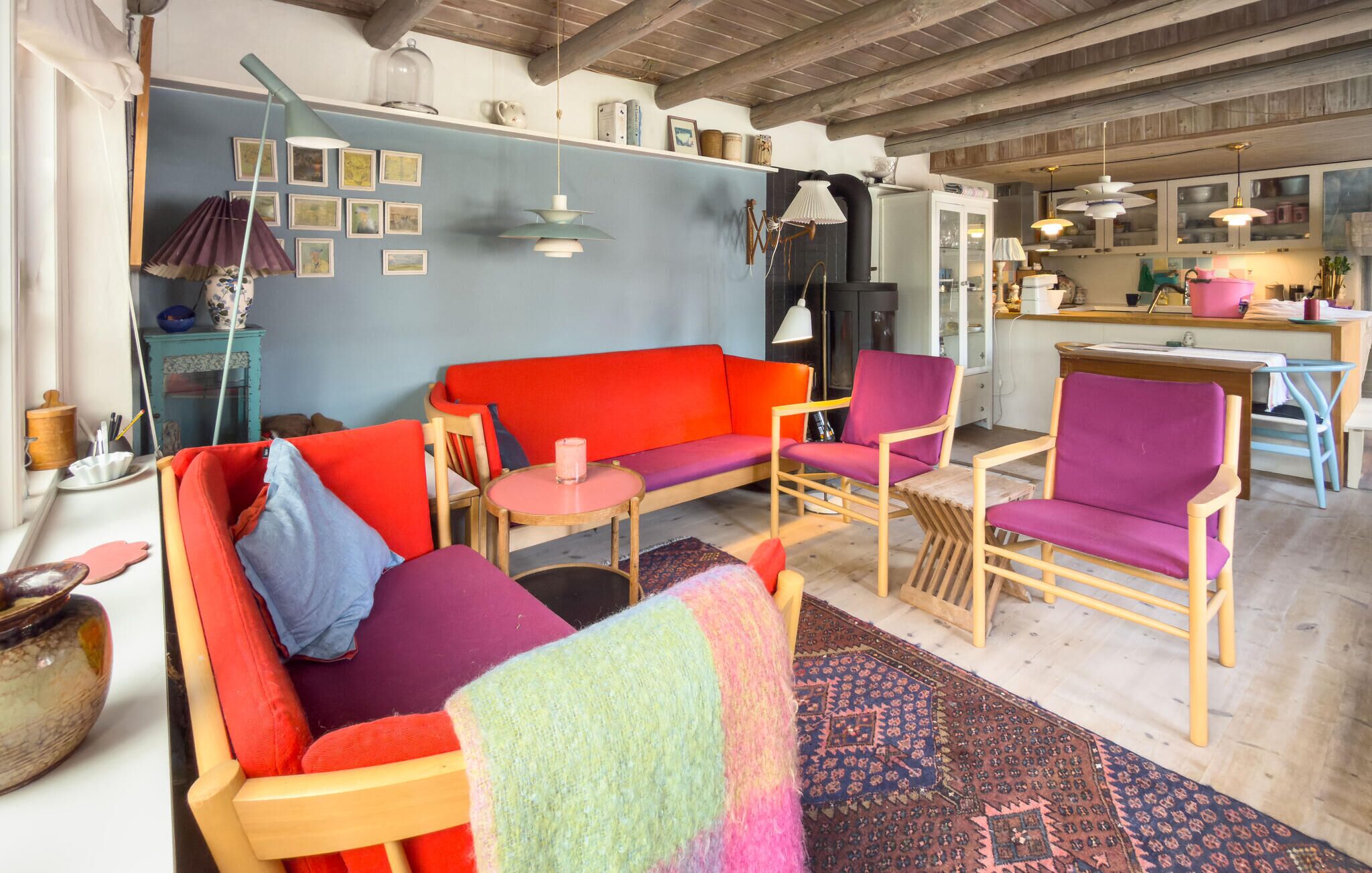 A cozy living room with a red sofa, purple chairs, a wooden coffee table, and a kitchen in the background.