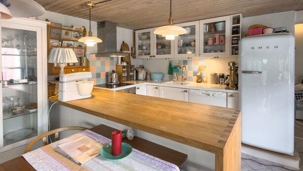 Eine Küche mit Holztischplatte, weißen Schränken, einem weißen Kühlschrank und einem Esstisch mit Unterlage und einer roten Kerze.