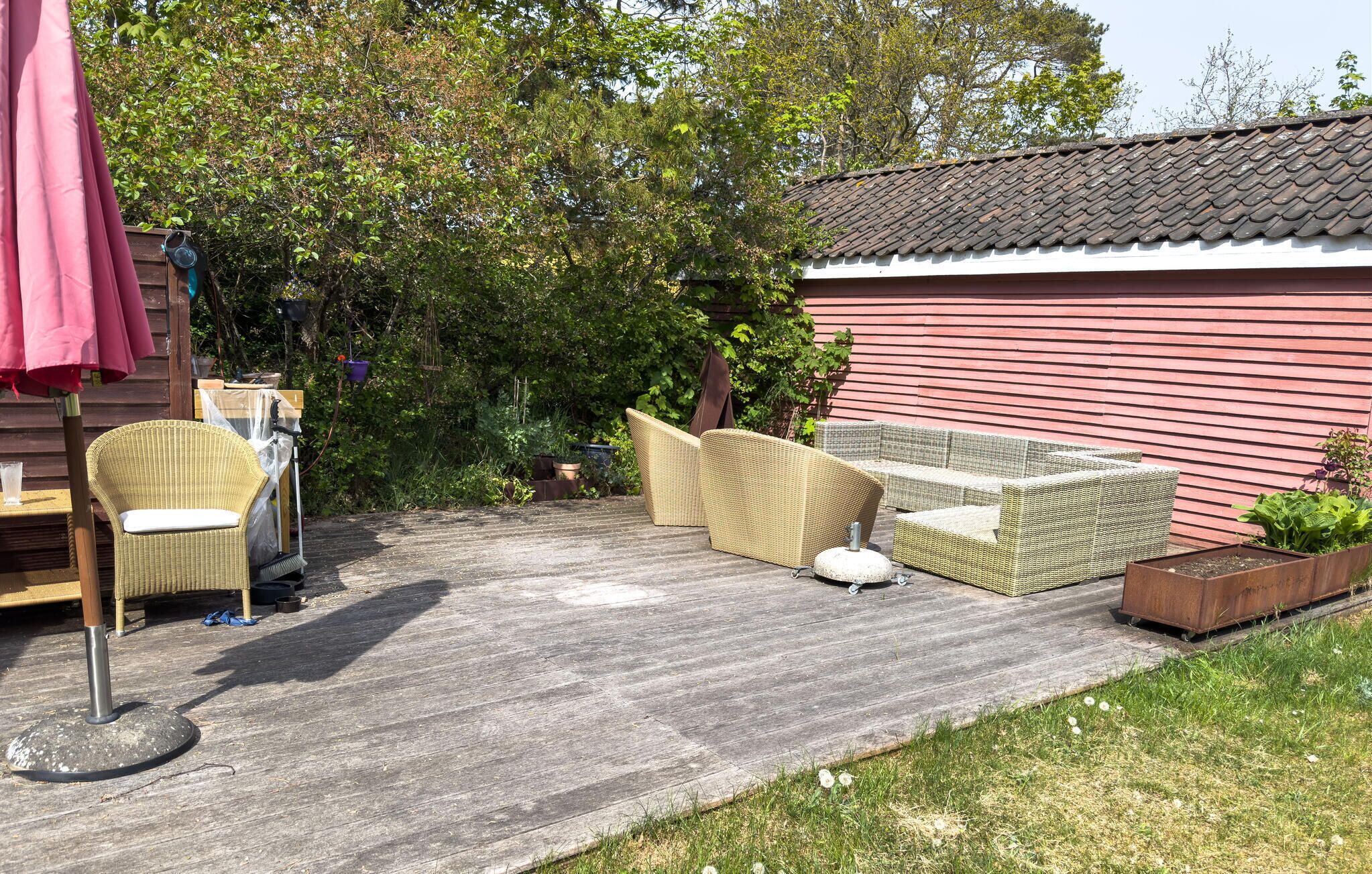 Een terras met rieten meubilair, een rood gebouw en een boom.