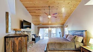 Ein Schlafzimmer mit Holzbalkendecke, einem Bett, einem Fernseher und einem Kamin aus Stein.