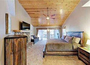 Ein Schlafzimmer mit Holzbalkendecke, einem Bett, einem Fernseher und einem Kamin aus Stein.