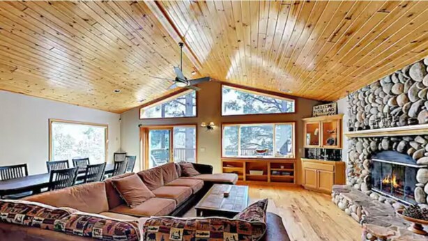 Ein gemütliches Wohnzimmer mit Holzboden, einem Kamin aus Stein und großen Fenstern.
