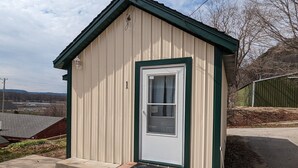 A small, single-story building with a white door and green trim, a small porch, and a clear sky in the background.