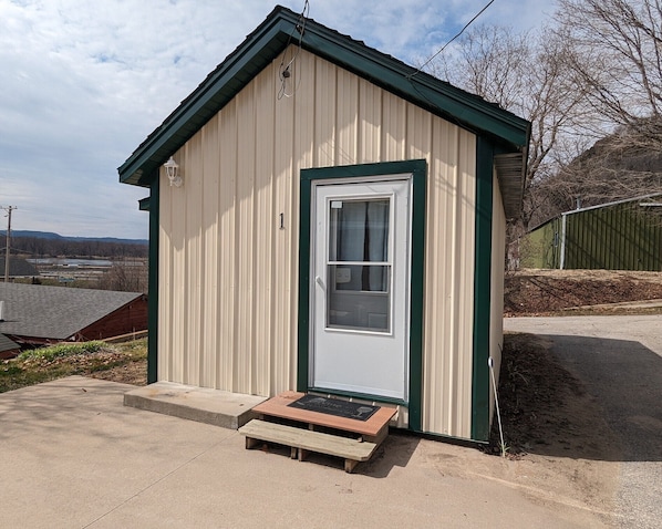A small, single-story building with a white door and green trim, a small porch, and a clear sky in the background. - Cozy 1 room cabin in De Soto! (De Soto)
