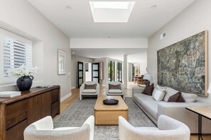 Ein geräumiges Wohnzimmer mit einer Couch, Sesseln, einem Couchtisch und einem Gemälde an der Wand.