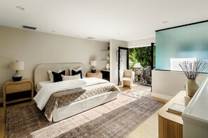 Ein modernes Schlafzimmer mit Bett, Nachttischen, einem Schreibtisch und Blick auf Grünflächen.
