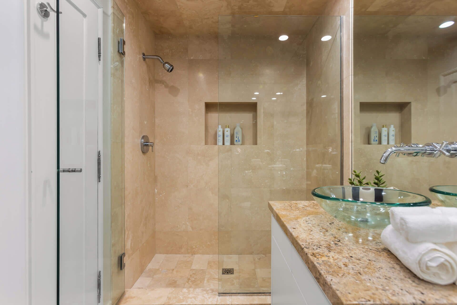 A modern bathroom with a glass-enclosed shower, a glass sink, and a mirror.