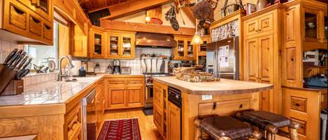 Una cocina con armarios de madera, una isla central, taburetes de bar y utensilios de cocina colgantes.