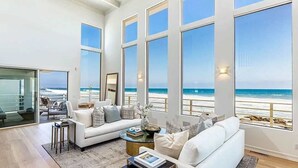 Un salón amplio con un gran ventanal con vistas a la playa, un sofá blanco, una mesa de centro y una mesita auxiliar.