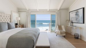 Un dormitorio con una cama grande, una silla, un escritorio y vista al océano.