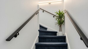 A staircase with dark carpeted steps, a handrail on each side, and a wall-mounted light fixture. - Charming 2-bedroom Apartment with AC in Yonkers (Yonkers)