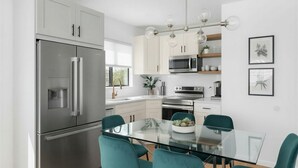 A modern kitchen with stainless steel appliances, teal chairs, and a glass dining table. - Charming 2-bedroom Apartment with AC in Yonkers (Yonkers)