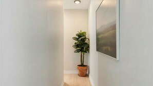 A hallway with a wooden floor, white walls, a potted plant, and a framed picture on the wall. - Charming 2-bedroom Apartment with AC in Yonkers (Yonkers)