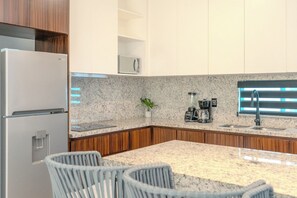 Una cocina moderna con refrigerador, microondas, cafetera y una ventana con persianas.