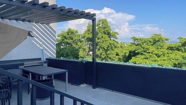 Une terrasse sur le toit, agrémentée d’une pergola, d’une table, de chaises et offrant une vue sur la verdure.
