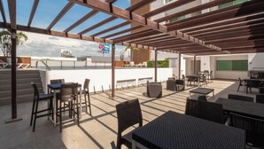 An outdoor patio area with tables and chairs, a pergola structure, and a view of the cityscape. - Spacious Apartment with Pool and BBQ Area (Mazatlan)