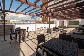 Ein Außenbereich mit Terrassentischen und -stühlen, einer Pergola und Blick auf die Stadt.