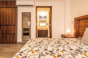 Ein Hotelzimmer mit einem Bett, einem Nachttisch, einer Lampe, einem Holzschrank, einem Spiegel und einer Klimaanlage.