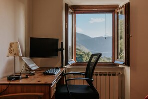 A room with a desk, a computer monitor, a keyboard, a chair, and a window with a view of mountains. - Ready to experience Italy in close proximity, sea, lakes and rivers? (Casciana)