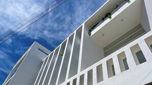 Een modern gebouw met witte muren, verticale lijnen en een balkon met planten.