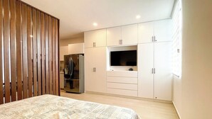 Een slaapkamer met een bed, een televisie, een koelkast en een kledingkast.