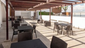 An outdoor patio with tables and chairs, a pergola structure, and a view of the sea. - Apartment for 6 on the first floor with pool (Mazatlan)