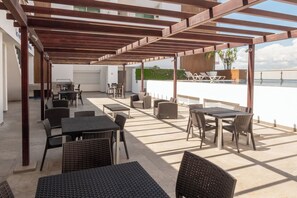 Eine Terrassengruppe mit Tischen und Stühlen, ein Pergola-Überdachung und Meerblick.