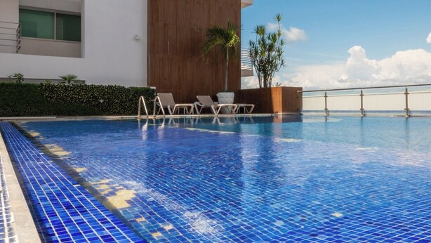 A swimming pool with tiled edges, lounge chairs, and a wooden wall. - Apartment for 6 on the first floor with pool (Mazatlan)
