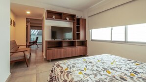 A bedroom with a bed, a TV, a wooden TV stand, a chair, and a window. - Apartment for 6 on the first floor with pool (Mazatlan)
