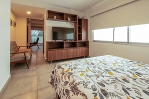 Ein Schlafzimmer mit Bett, Fernseher, Holz-TV-Möbel, einem Sessel und einem Fenster.