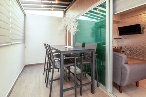 Ein modernes Zimmer mit Esstisch, Stühlen, einer Couch, einem Fernseher und einer Zimmerpflanze.