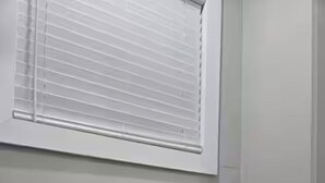 A bathroom with a toilet, a window with blinds, and a wall.