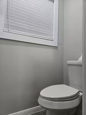A bathroom with a toilet, a window with blinds, and a tiled floor.