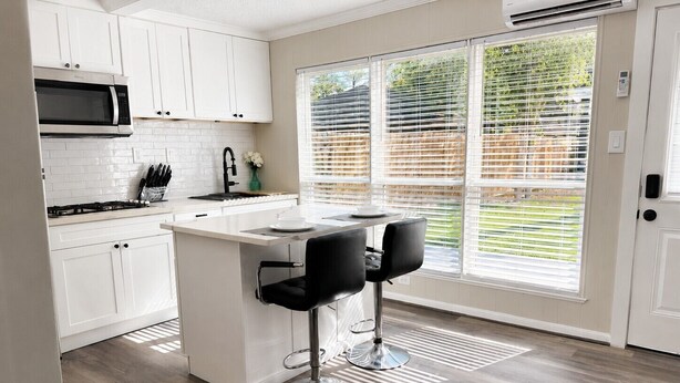 A modern kitchen with white cabinets, a built-in microwave, a gas stove, and a large window with blinds.