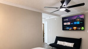A bedroom with a bed, a black sofa, a ceiling fan, and a TV displaying a home screen.