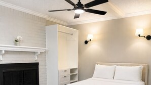 A bedroom with a bed, a ceiling fan, a fireplace, and a wall-mounted light fixture.