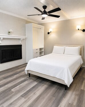 A bedroom with a bed, a ceiling fan, a fireplace, and a wall-mounted light fixture.