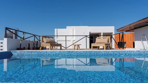 Una piscina en la azotea con dos sillones de madera, una mesita y plantas en macetas.