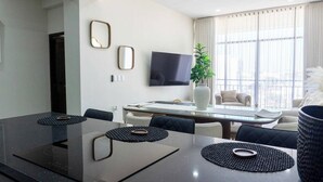 Una sala de reuniones moderna con una mesa de vidrio, sillas negras, un televisor de pantalla plana y un amplio ventanal con cortinas.