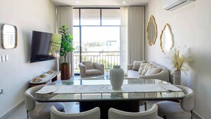 Una sala moderna con una mesa de comedor de cristal, asientos cómodos, un televisor de pantalla plana y un balcón con vistas.