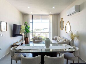 Ein modernes Wohnzimmer mit einem Glastisch, bequemen Sitzmöglichkeiten, einem Flachbildfernseher und einem Balkon mit Aussicht.