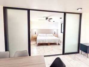 Een moderne slaapkamer met een bed, nachtkastjes, een plafondventilator en een schuifdeur die leidt naar een eethoek.