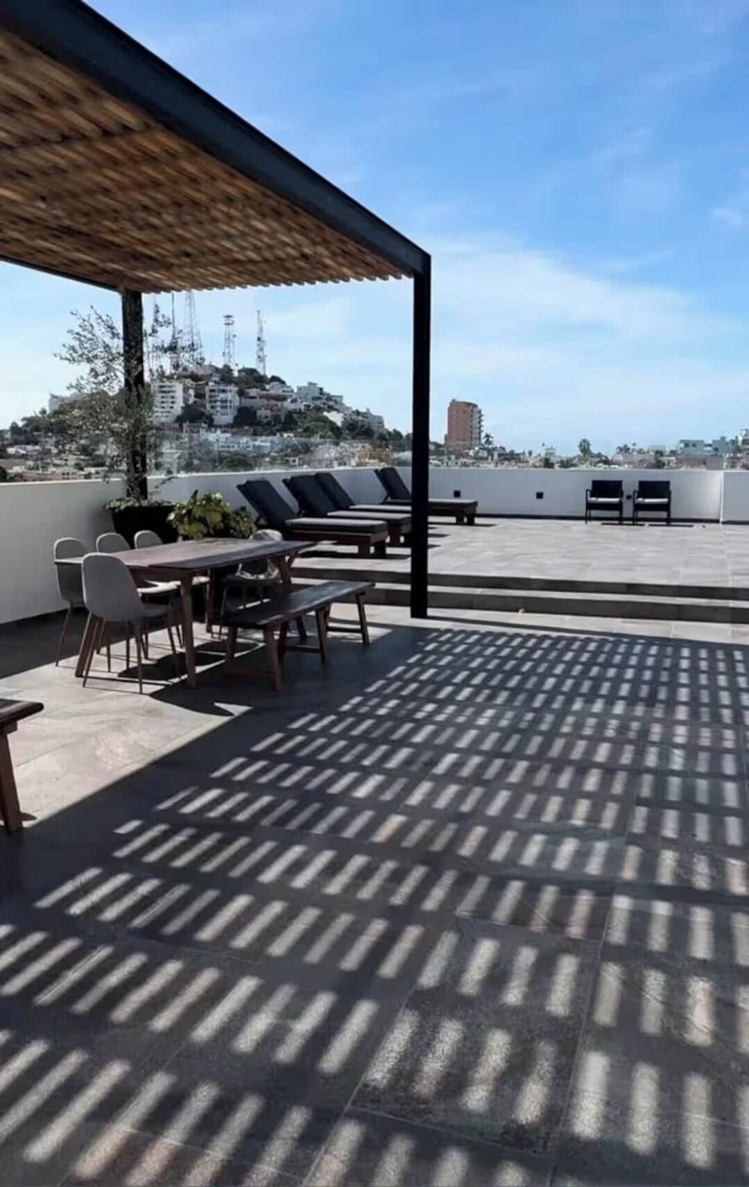 A rooftop terrace with a covered seating area, a table, and chairs.